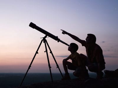 Two people in silhouette with a telescope