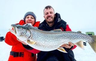 An accomplished Manitoba fishing guide holds up a catch while smiling with his student.