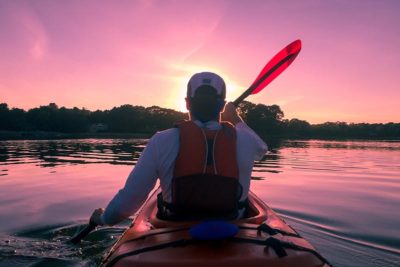 man kayaking on a lake at sunset.