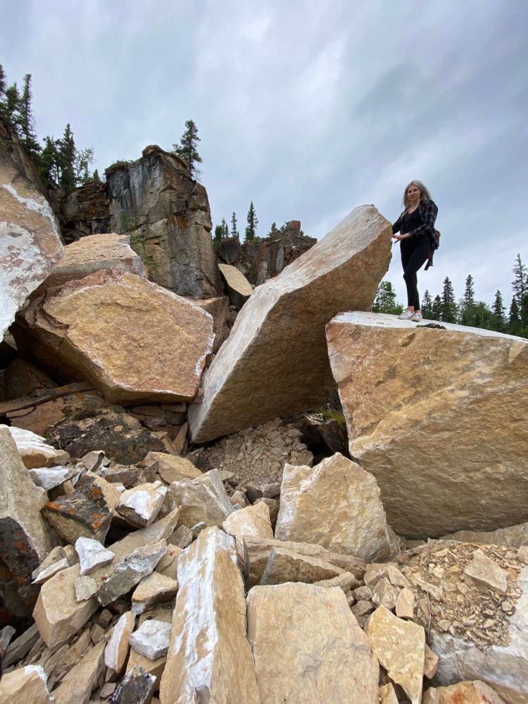 A curious explorer scales a group of large limestone boulders while hiking in Manitoba.