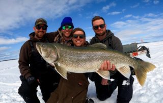 Four fishing buddy's holding a massive lake trout showing why Bakers Narrows is among the best bachelor party destinations in Canada.