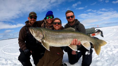 Four fishing buddy's holding a massive lake trout showing why Bakers Narrows is among the best bachelor party destinations in Canada.