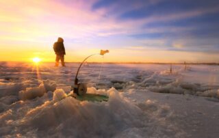 Ice Fishing Vacation Packages: An avid angler stands in the sunrise while ice fishing in Manitoba.