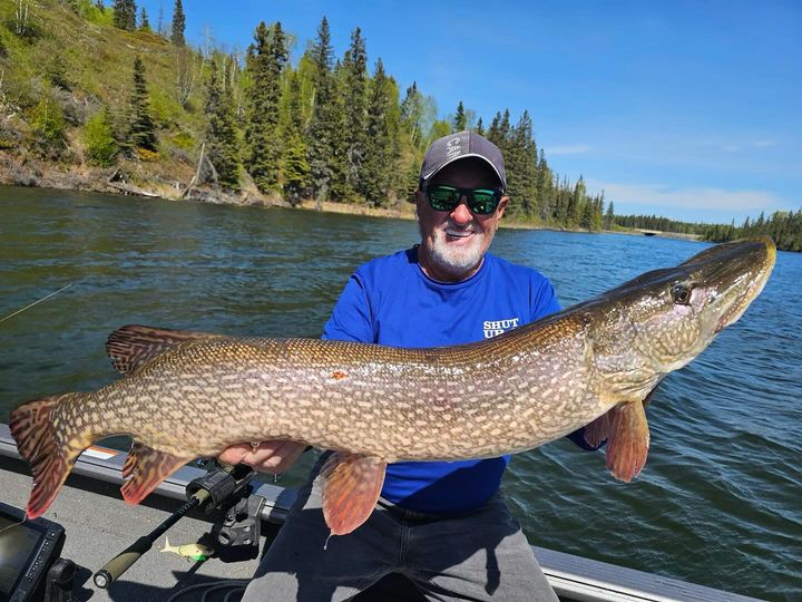 Canada Fishing Trips: An avid angler smiles as he hoists a large northern pike while fishing on Lake Athapapuskow.